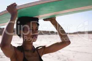 Young African American woman carrying the surfboard on her head at beach