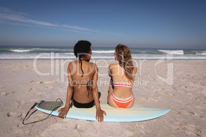Young women sitting on surfboard at beach in the sunshine