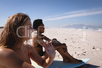 Happy young women sitting on surfboard at beach in the sunshine