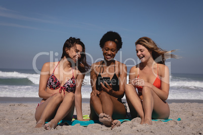 Happy young women using mobile phone while sitting at beach