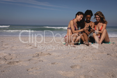 Happy young women using mobile phone while sitting at beach