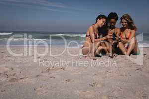 Happy young women using mobile phone while sitting at beach