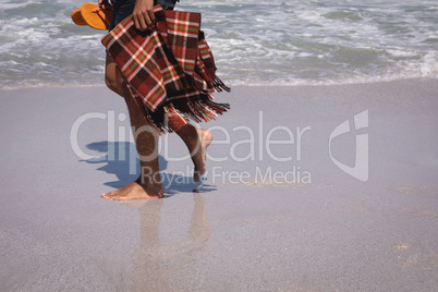 Man holding blanket and slipper while walking on beach in the sunshine