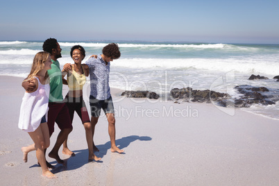 Happy group of friends walking on beach with arms around the waist