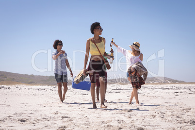 Group of friends carrying ice box and beer bottles on beach in the sunshine