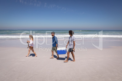 Group of friends carrying ice box and beer bottles on beach in the sunshine