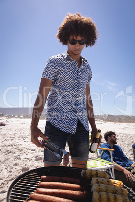 Young man cooking Corn and sausage on barbecue at beach in the sunshine