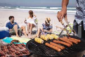 Mid-section of a man doing a barbecue while his friends in background at beach