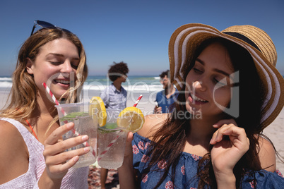 Beautiful young woman toasting cocktail glasses at beach in the sunshine