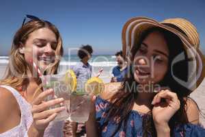 Beautiful young woman toasting cocktail glasses at beach in the sunshine