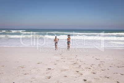 Shirtless young men running on beach in the sunshine