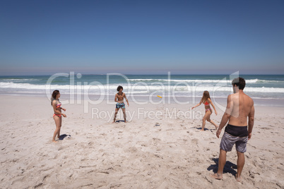 Group of friends playing with Frisbee on beach in the sunshine