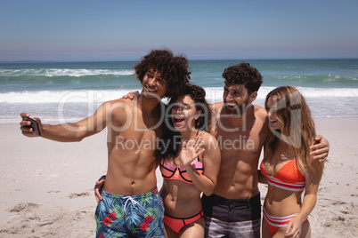 Group of friends taking selfie with mobile phone at beach in the sunshine