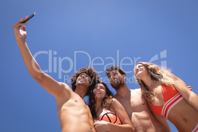 Group of friends taking selfie with mobile phone at beach in the sunshine