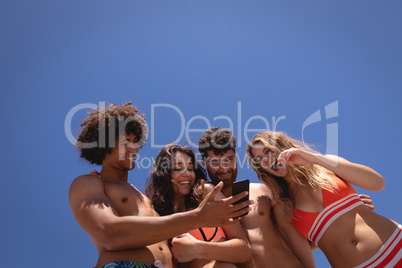 Happy group of friends reviewing photos on mobile phone at beach in the sunshine