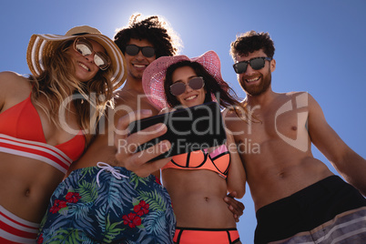 Group of friends taking selfie with mobile phone at beach in the sunshine