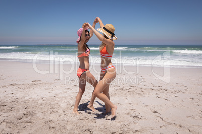 Beautiful young women with hat and sunglasses dancing at beach in the sunshine