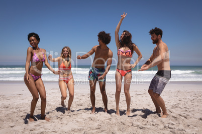 Happy group of friends dancing together on beach in the sunshine