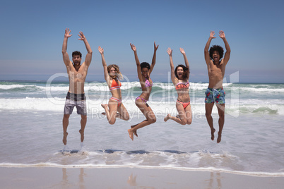Happy group of friends jumping together on beach in the sunshine