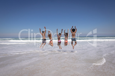 Happy group of friends jumping together on beach in the sunshine