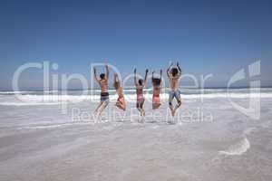 Happy group of friends jumping together on beach in the sunshine