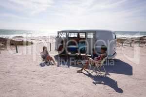 Group of friends relaxing near a camper van at beach in the sunshine