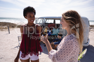 Happy young women drinking beer bottle against friends sitting near a camper va