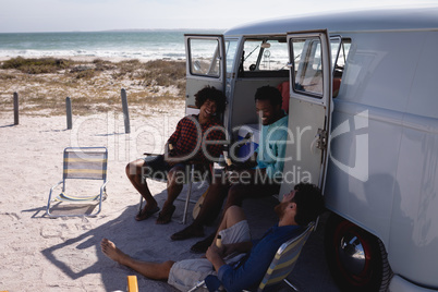 Happy young men relaxing near camper van at beach in the sunshine