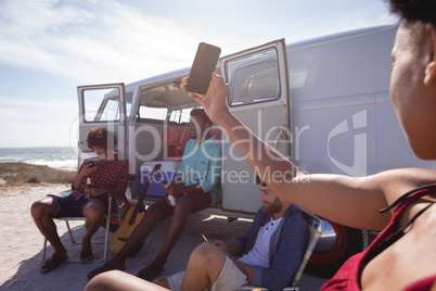 Mid-section of a woman looking for WiFi while his friends are sitting near camper van