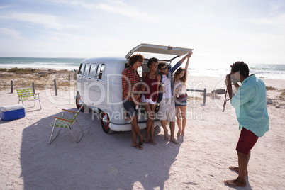 Man capturing photos of his friends sitting in the trunk of a camper van