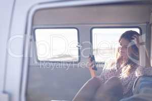 Beautiful thoughtful woman using mobile phone in camper van at beach