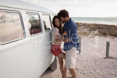 Side view of a Caucasian couple leaned on a camper van while they hugging themselves against ocean i