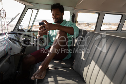 Man using mobile phone in camper van at beach