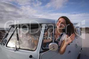 Woman having his head outside the camper van while she is waving out by window