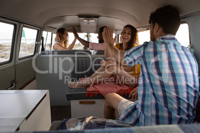 Group of friends giving high five in camper van at beach