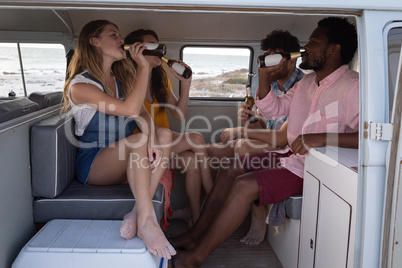 Group of friends sipping beers in camper van at beach