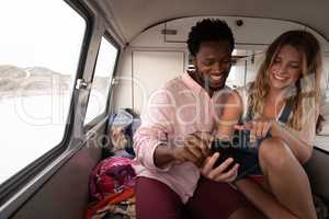 Couple laughing while they are using mobile phone in camper van at beach