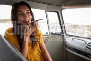 Beautiful woman talking on mobile phone in camper van at beach