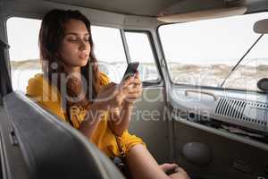 Beautiful woman using mobile phone in camper van at beach