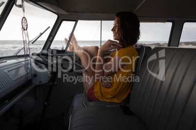 Beautiful woman relaxing in camper van with his foot outside against beach in background