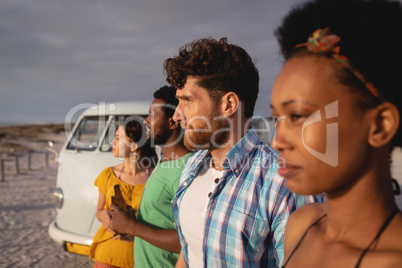 Friends group standing in raw on sand while they are looking away ocean