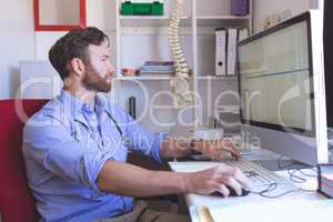 Confident male doctor working on computer in clinic