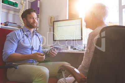 Male doctor using digital tablet while talking with senior woman in clinic