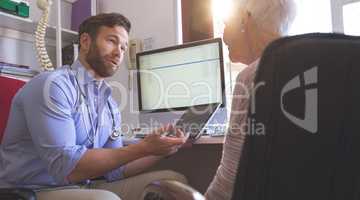 Male doctor using digital tablet while talking with senior woman in clinic
