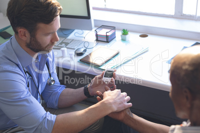 Confident male doctor examining senior man with glucometer in clinic