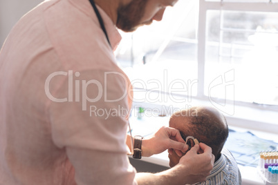 Male doctor applying hearing aid to senior man ear