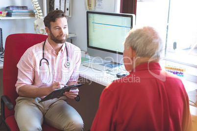 Male doctor talking to senior patient while holding medical report