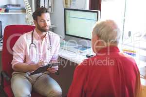 Male doctor talking to senior patient while holding medical report