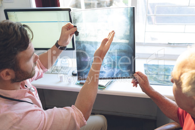 Confident male doctor showing x ray to senior patient in clinic