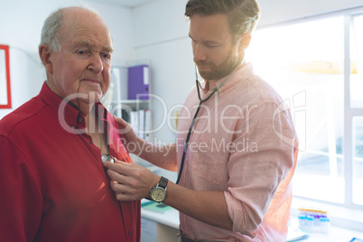 Confident male doctor checking senior patient heartbeats in clinic